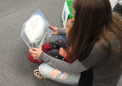 A teenage girl reading a picture book to a little girl.
