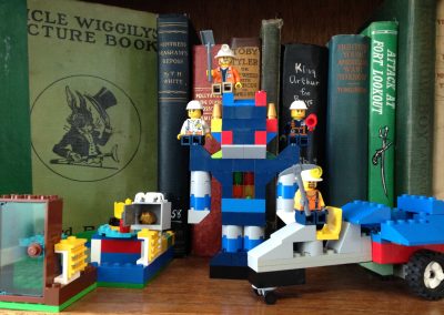 Objects built with Lego bricks in front of a shelf of books.